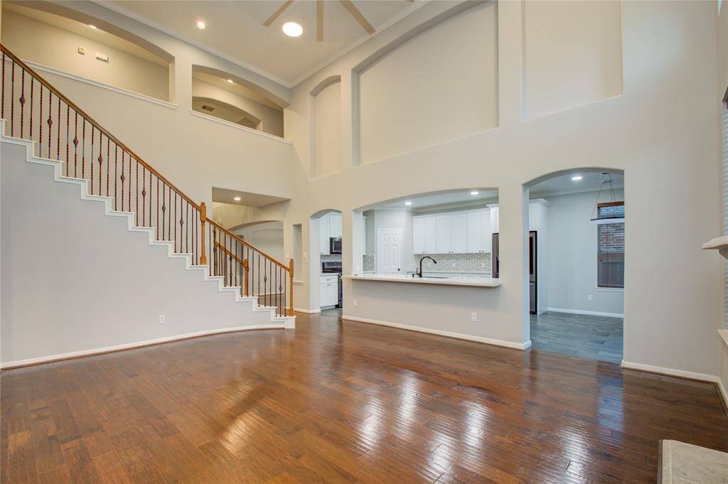 Spacious, open-concept living area features high ceilings, elegant hardwood floors, and a grand staircase.