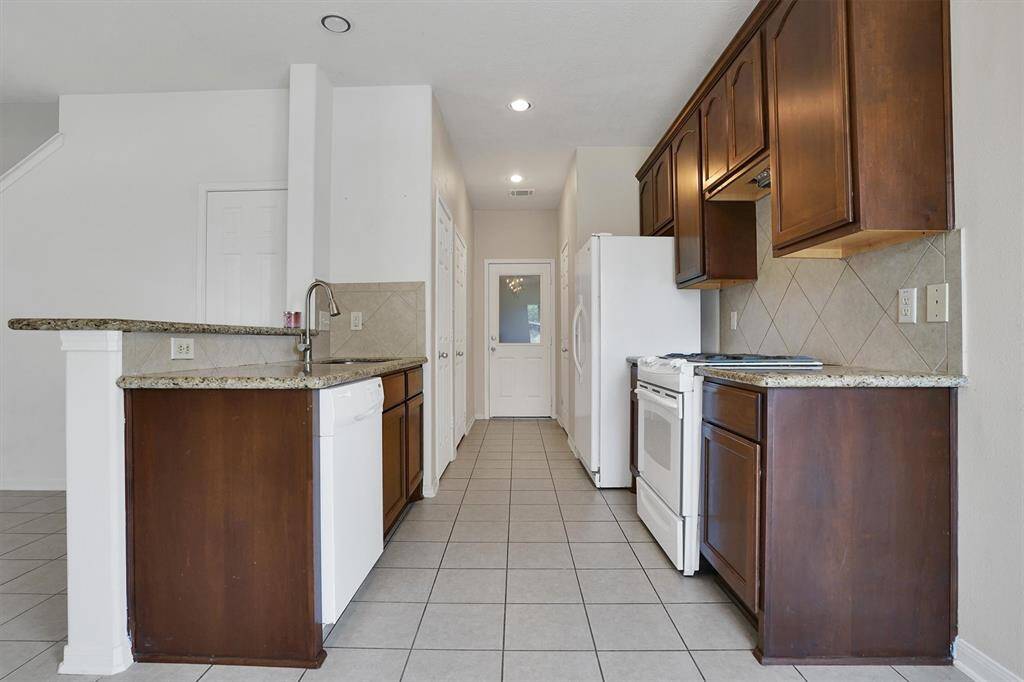 This kitchen features sleek countertops, rich wood cabinetry, and modern appliances. The neutral tile flooring and backsplash add a clean, spacious feel, while ample lighting enhances functionality.