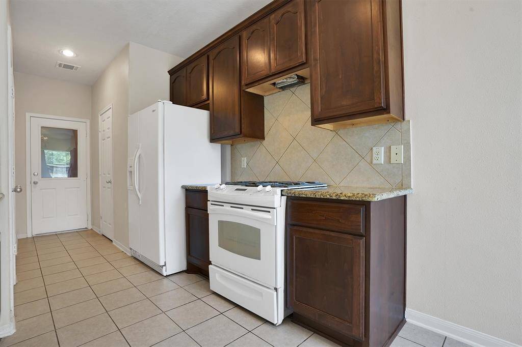 This kitchen features tiled floors, dark wood cabinets, and countertops. It includes a white refrigerator and stove, with a tiled backsplash. There's a door leading outside, offering natural light.
