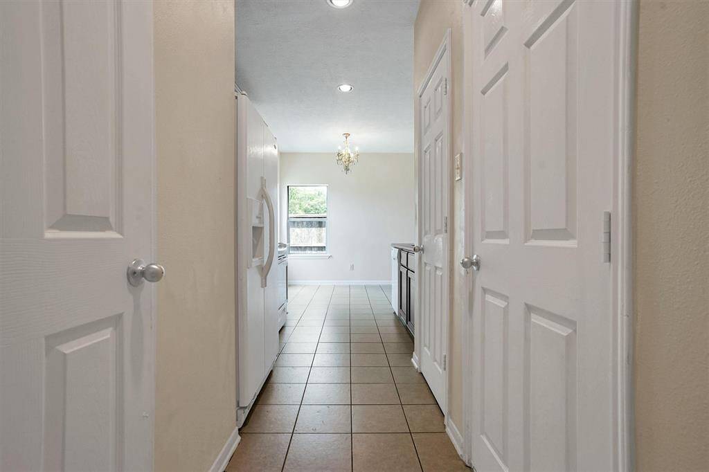 This photo shows a bright kitchen with tiled floors, a white refrigerator, and ample cabinet space. It features a small window and a chandelier, providing natural light and elegance.