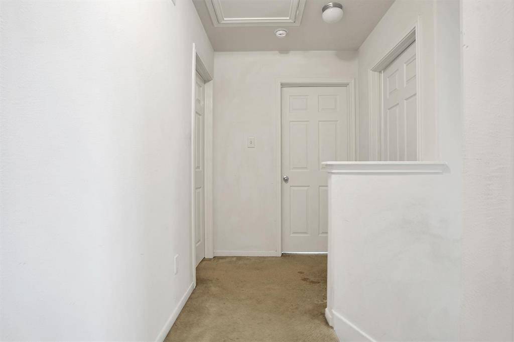 Bright hallway with white walls and carpeted floor, featuring multiple doors and a ceiling light.
