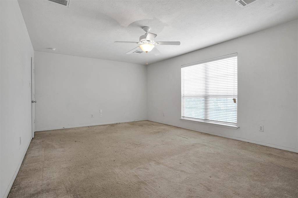 This is a spacious, empty room with neutral walls, and a large window with blinds, offering plenty of natural light. It has carpeted flooring and appears ready for personal touches.