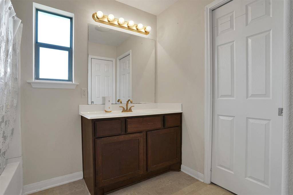 This bathroom features a sleek vanity with a large mirror, modern lighting, and a window for natural light. The neutral color palette creates a clean and inviting atmosphere.
