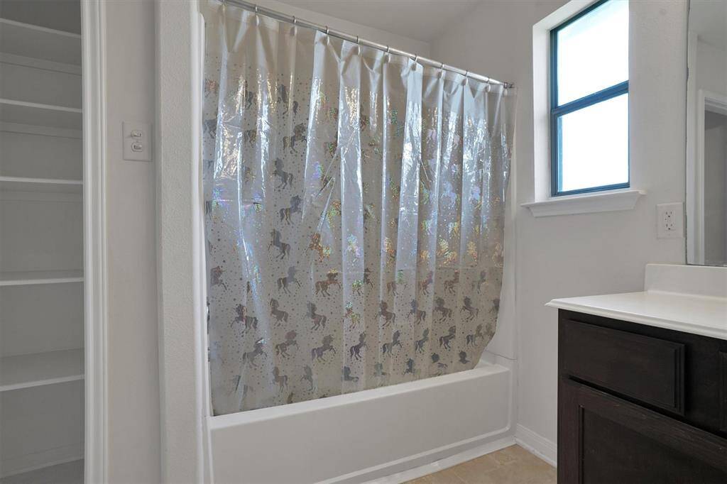 This bathroom features a bathtub, a window for natural light, and a vanity with dark cabinetry. There’s also a built-in shelving unit for storage.