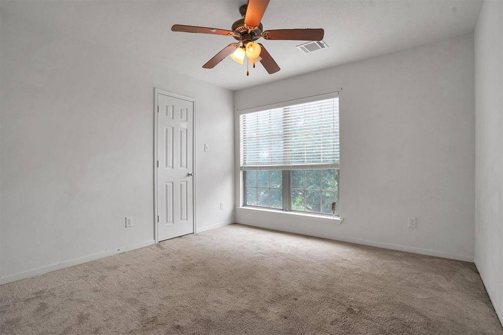 This is a cozy bedroom with neutral walls and carpet flooring and a small closet with a paneled door.