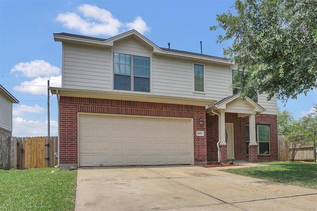 This two-story home features a spacious driveway, a brick and siding exterior, and a two-car garage. The property is surrounded by a well-kept lawn and a wooden fence, offering privacy and a welcoming entrance.