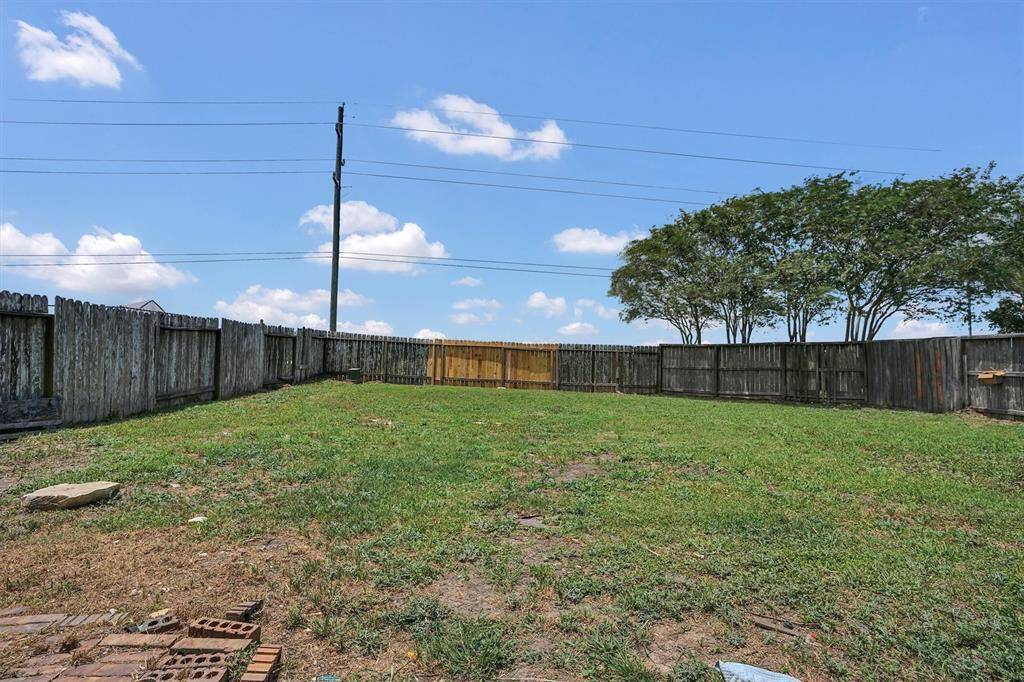 Spacious backyard with a mix of grass and bare patches, enclosed by a wooden fence. Ideal for landscaping or outdoor activities.
