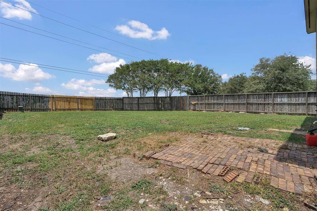 Spacious backyard with a mix of grass and a small brick patio area, enclosed by wooden fencing, offering privacy and potential for landscaping or outdoor activities.