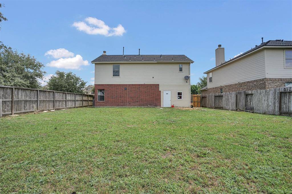 This photo shows a spacious backyard with a well-maintained lawn, enclosed by a wooden fence. The back of a two-story house with a mix of brick and siding is visible, offering a simple, clean exterior. Perfect for outdoor activities and privacy.