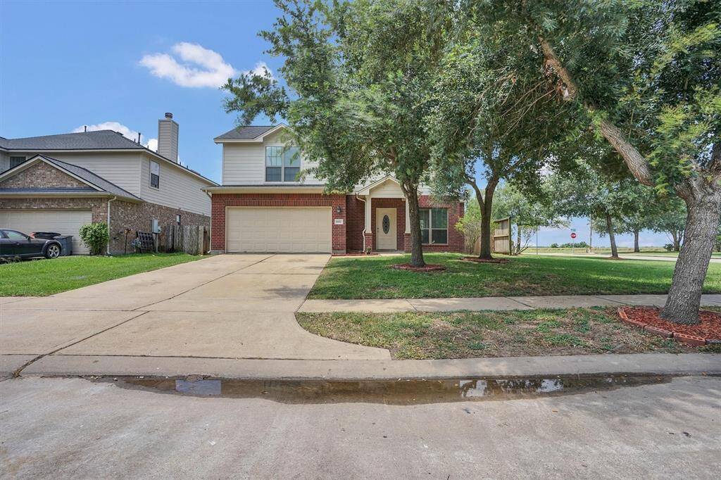 This two-story home features a brick and siding exterior with a large driveway and two-car garage. It is surrounded by mature trees and has a well-maintained lawn, creating a welcoming curb appeal.