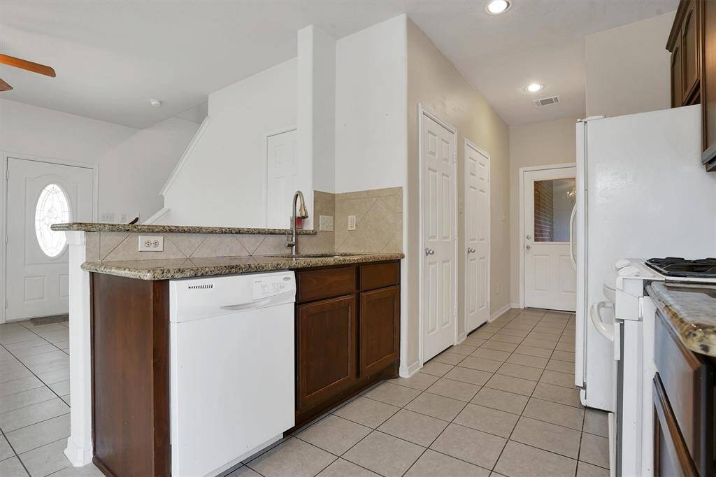 Bright kitchen with tile flooring, countertops, and wooden cabinetry. Features a dishwasher, gas stove, and refrigerator. The layout includes a breakfast bar, pantry, and easy access to the entryway and stairs.
