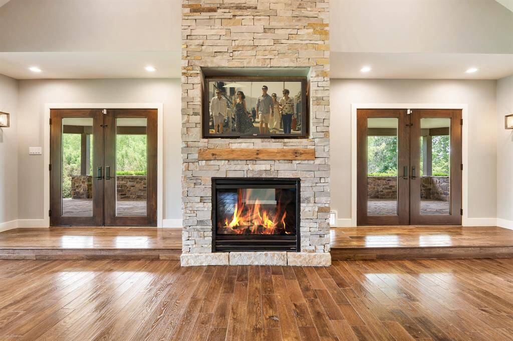 A perfect blend of textures and soothing warm colors provides the ideal pallet for the floor-to-ceiling stacked stone fireplace finished with a cedar mantel and pre-wired for an inset TV. Notice how the raised landings accentuate the 2-sets of double glass doors that open to the covered Porch.