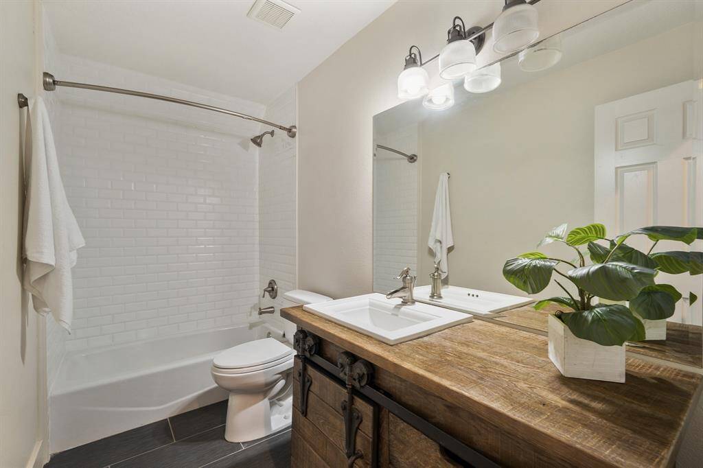 The upstairs Bath is finely finished and captures the essence of a country home with a designer vanity with a ceramic sink inset in a wood countertop and cabinet doors on a metal sliding track. Beautiful slate gray 12x24 tiles coordinate with the white subway tile tub/shower.