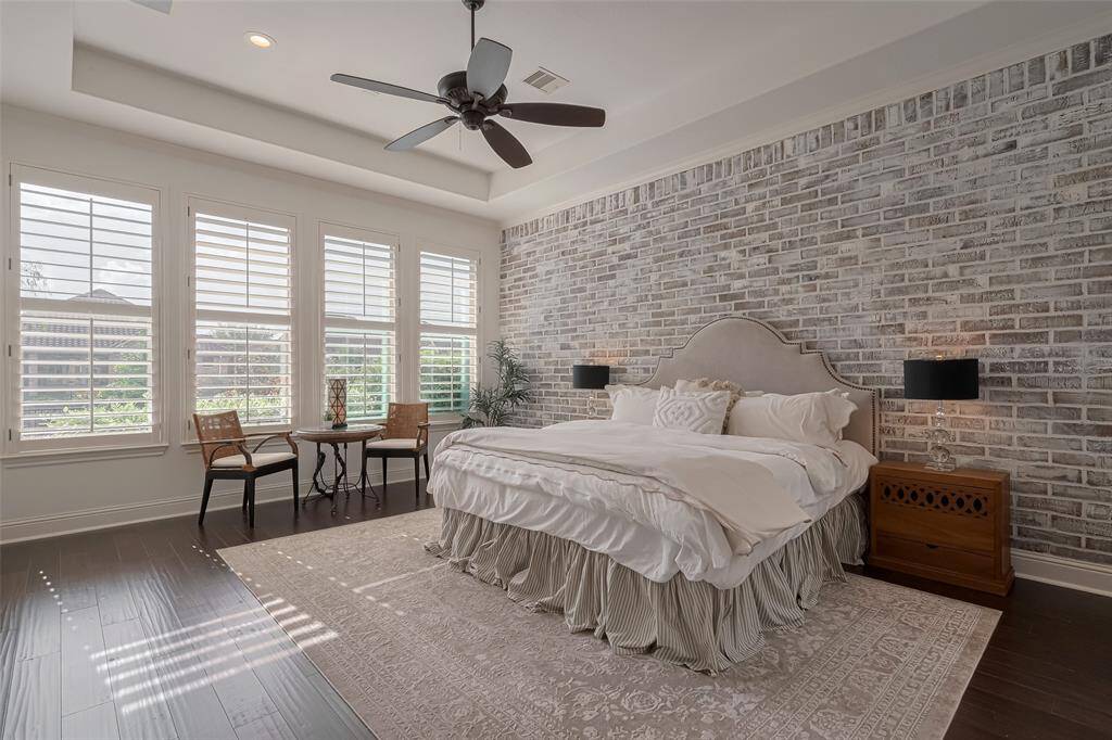Primary bedroom with recessed tray ceiling, recessed LED lighting on dimmers added, faux brick wall custom painted, Plantation shutters, ceiling speakers, eng wood floors.