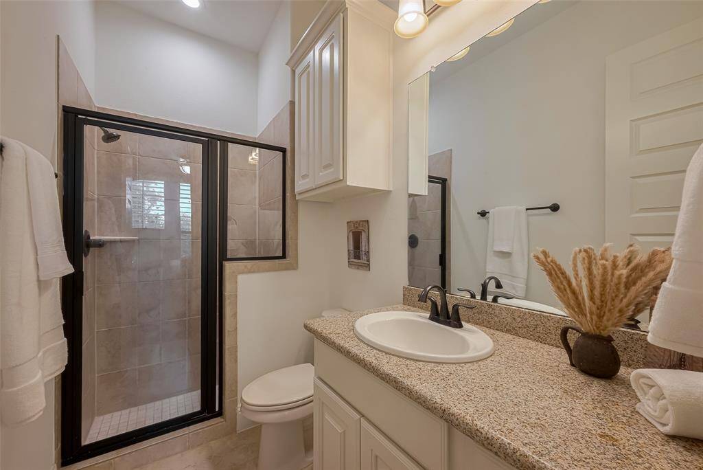 This bathroom is the ensuite bath to the prior bedroom photo, tile floors, granite counters, additional built in storage above toilet, tiled shower with bench, oil rubbed bronze hardware, recessed LED lighting.