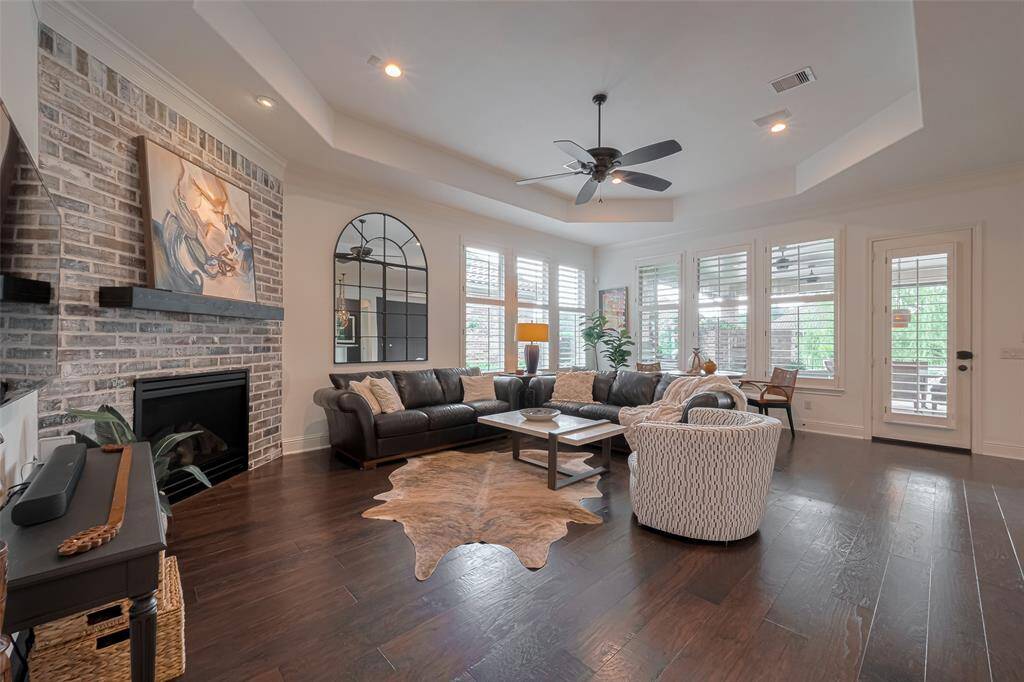 Living room with gas log fireplace, eng. wood floors, tray ceiling, double pane windows with Plantation shutters, recessed LED lighting on dimmers, ceiling fan and speakers in ceiling.
