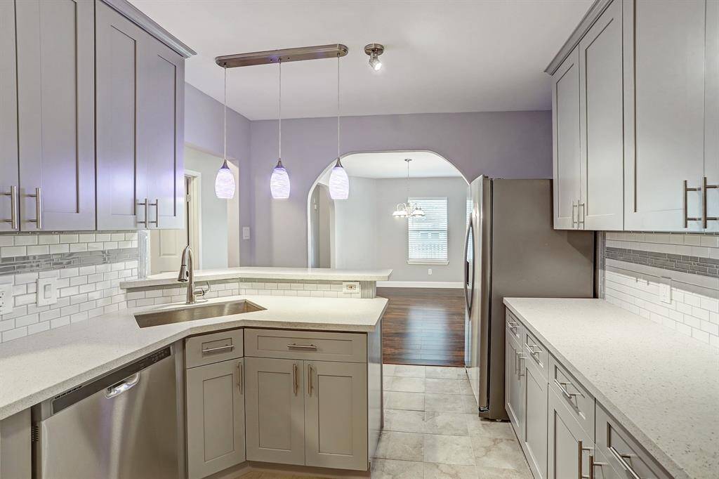 This is a modern kitchen with gray cabinetry, stainless steel appliances, subway tile backsplash, and quartz countertops. It features pendant lighting and has a view into an adjoining dinning room through an arched opening.