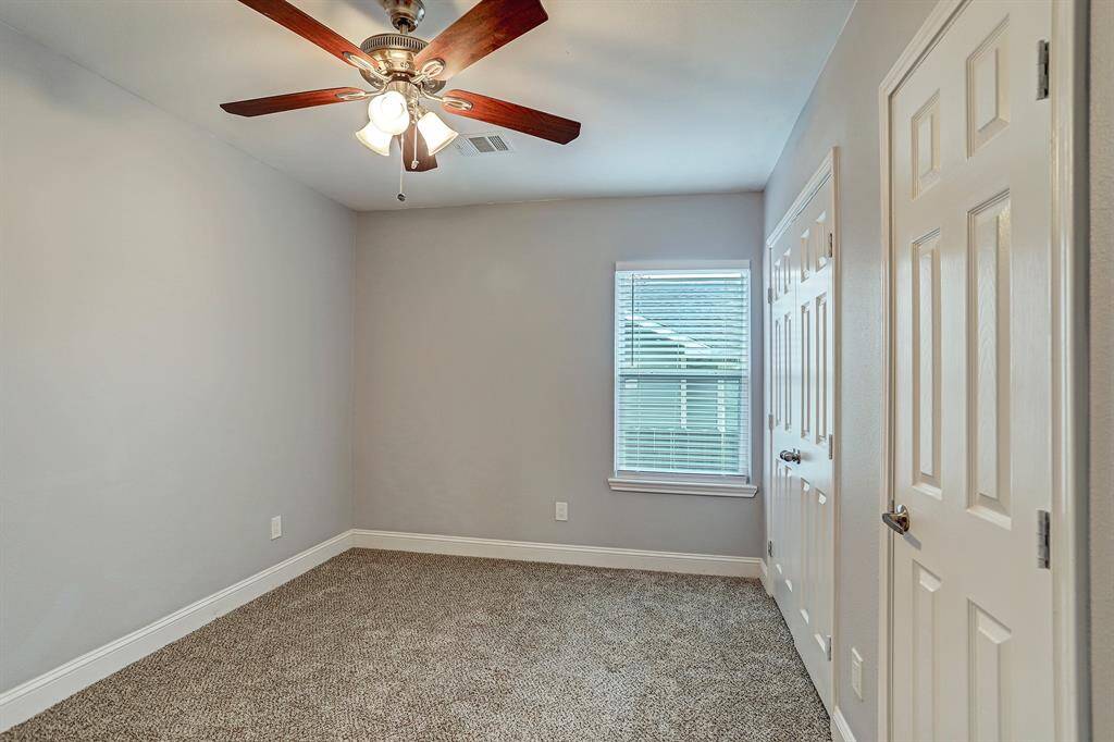 This first bedroom features carpet flooring, a ceiling fan with lighting, and ample closet space.