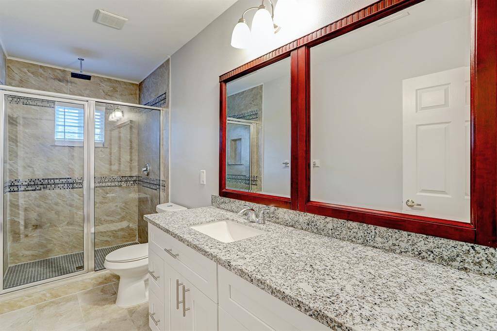 This bathroom features a large walk-in shower enclosed by glass doors, a single vanity with generous counter space and white cabinetry, topped with a quartz countertop.