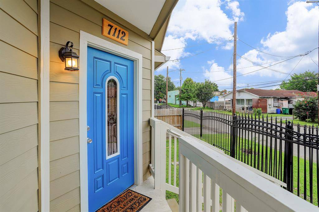 The entry features a porch with a railing, overlooking a fenced front yard.