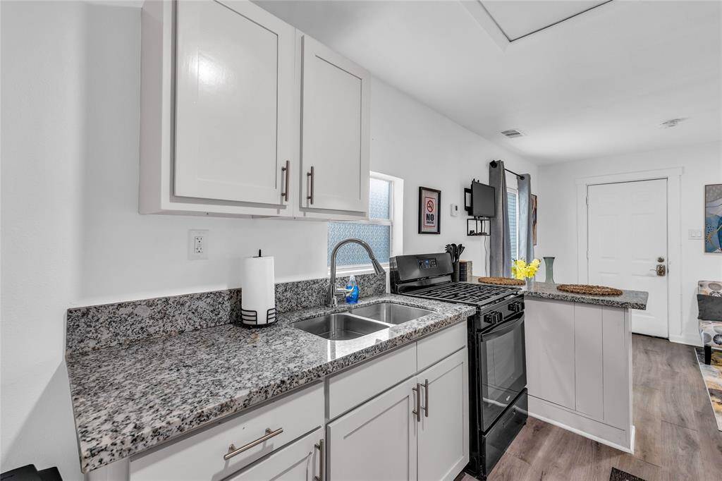This is a modern, compact kitchen featuring white cabinetry, granite countertops, stainless steel sink, and black stove.