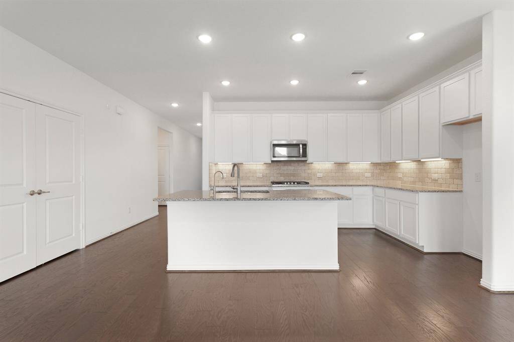 Open-concept Kitchen features a large center island with sink and bar seating, granite countertops, and ample white cabinetry. The warm subway tile backsplash adds a stylish touch.