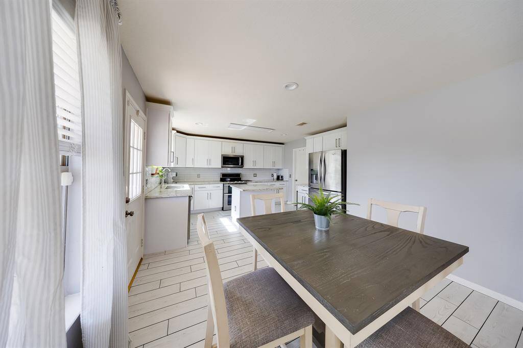 Bright breakfast area opens to modern kitchen with stainless steel appliances and white cabinets.