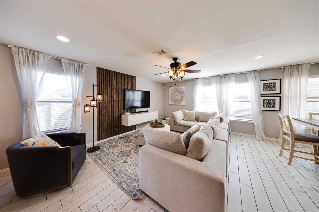 Bright living room with large windows, stylish accent wall, and cozy neutral-toned sectional perfect for relaxing.