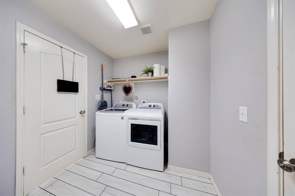 Functional laundry room with full-size washer and dryer, built-in shelf, and tile flooring.