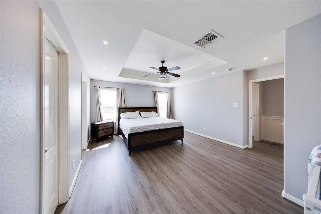 Primary bedroom boasts luxury tray ceiling and sleek wood flooring.