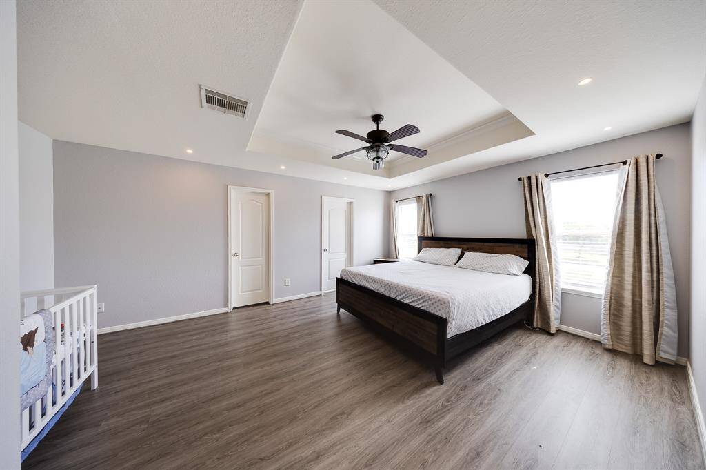 The spacious primary bedroom features a stylish tray ceiling, modern gray tones, and rich laminate flooring that adds warmth and elegance.