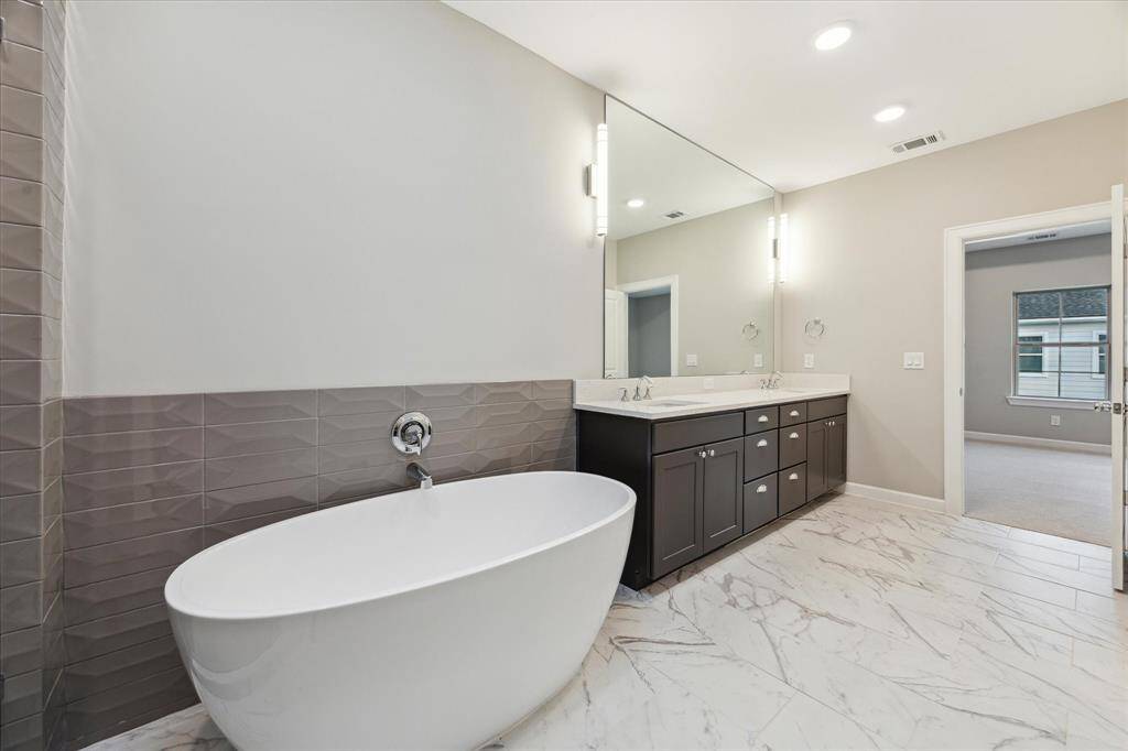 View of primary bath showcasing dual sinks, ample storage, and marble-style tile flooring.