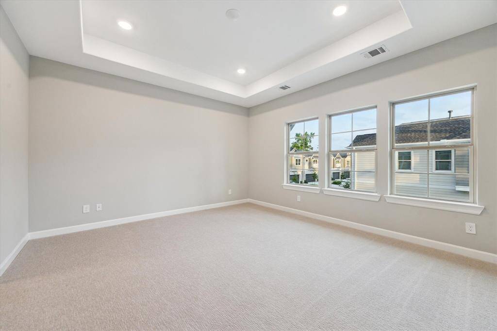 Primary suite featuring tray ceiling, lush carpet, and oversized windows.
