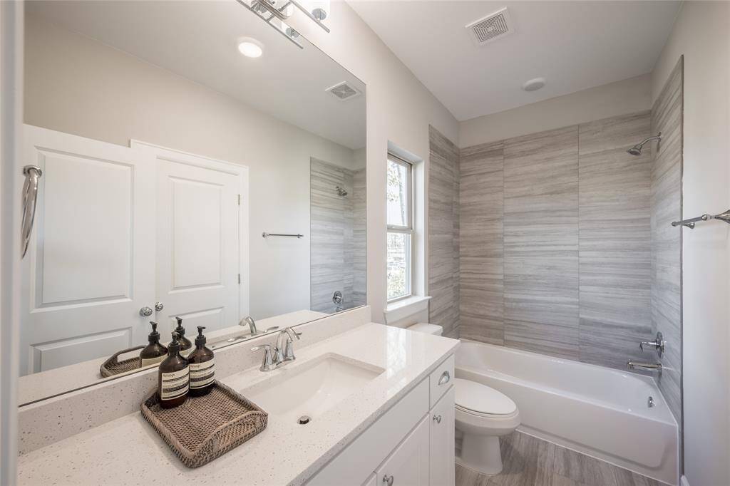 eatures modern tile surround, quartz vanity, and a window for natural light.