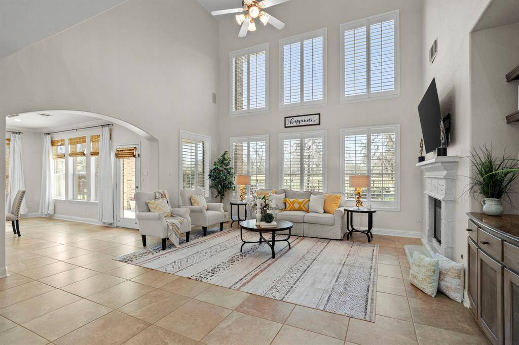 Living room features tile flooring, aceiling fan, high ceilings, and a wallof windows.