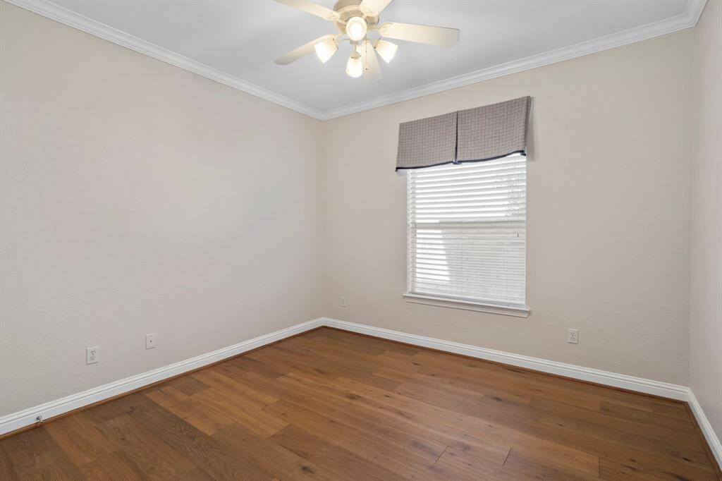 Sixth bedroom on the first floor features awindow, ceiling fan, crown molding, and beautiful floors.