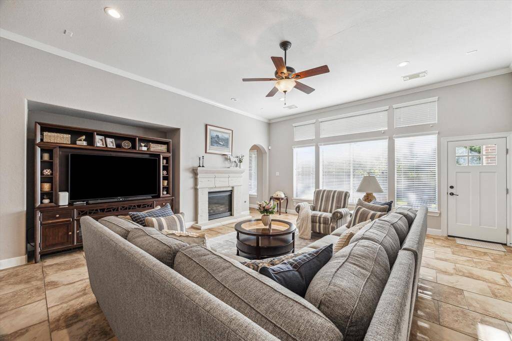 This spacious living room features a charming fireplace. The room is filled with natural light from large windows and has a ceiling fan for comfort. It offers a welcoming, open atmosphere perfect for relaxation and entertainment.