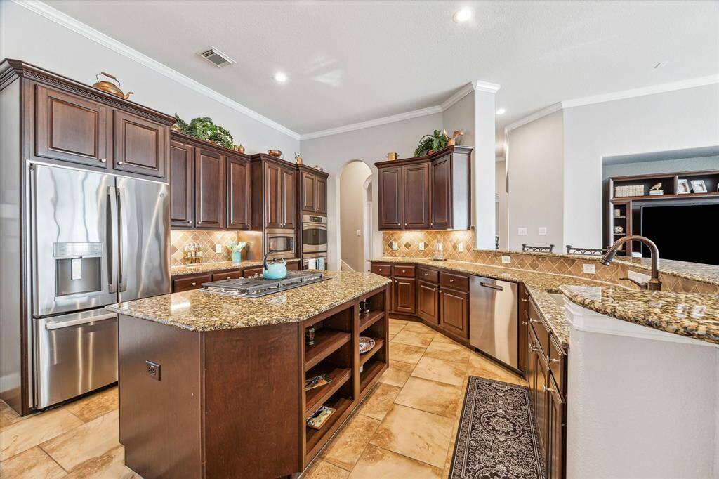 Appliances, including a double oven and large refrigerator. An island with a cooktop adds functionality, while the open layout and tile flooring enhance the space's elegance.