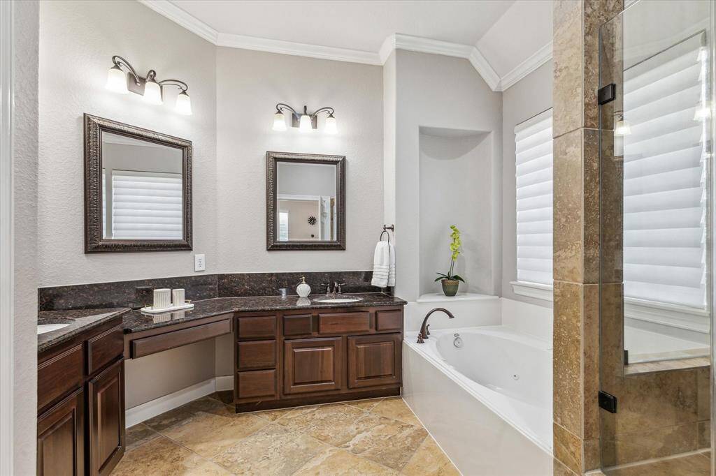 This elegant bathroom features dual sinks with dark wood cabinetry and granite countertops. It includes a spacious soaking tub, a separate glass-enclosed shower, and stylish lighting fixtures, creating a luxurious and functional space.