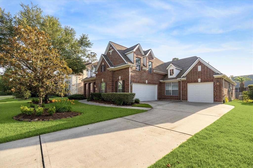 A spacious, two-story brick home with a well-maintained lawn and a three-car garage. The driveway is wide, and there are mature trees and shrubs enhancing the curb appeal. The house features multiple gables and large windows, adding to its elegant appearance.