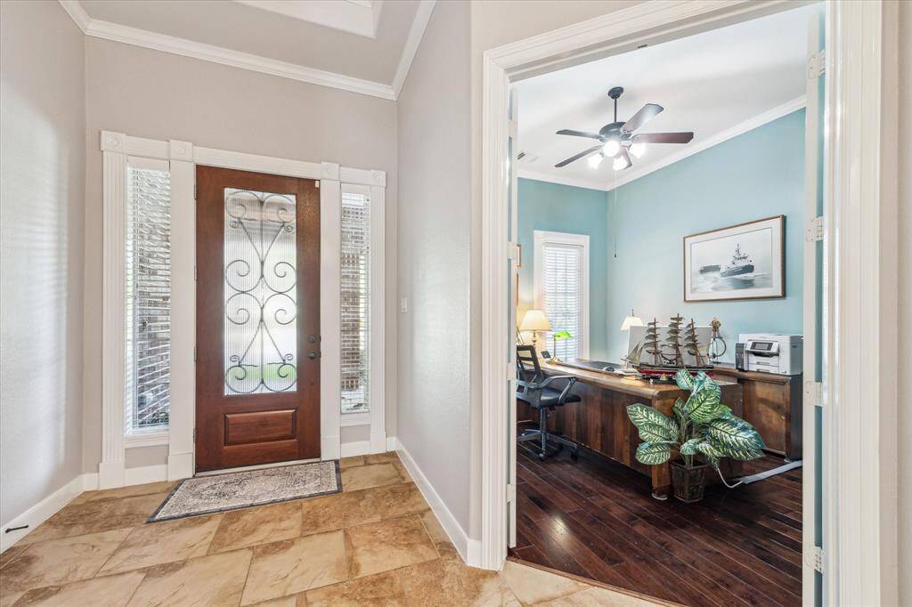 A welcoming entryway with a decorative glass front door and tiled flooring. To the right, there's a cozy office with hardwood floors, a ceiling fan, and ample natural light.