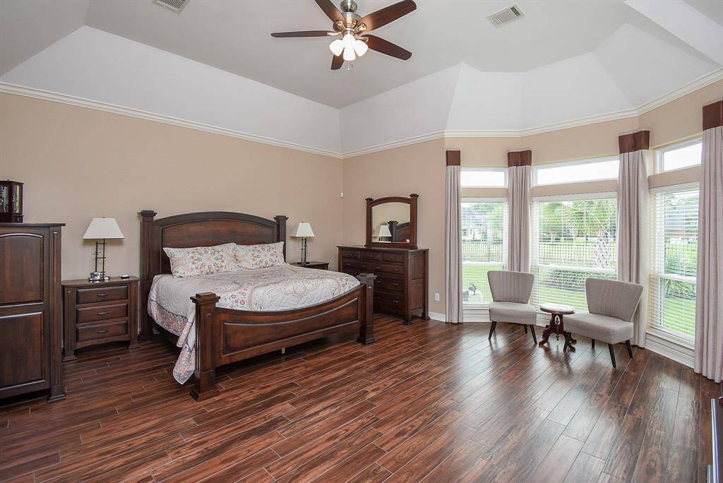 Massive primary suite with new wood tile flooring, updated lighting, ceiling fan, freshly painted walls with windows overlooking the pool, spa and lake.