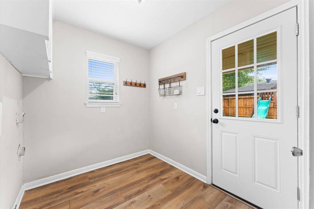 Bright utility room with luxury vinyl flooring, neutral walls, and a window. Door leads to a fenced backyard, perfect for easy outdoor access.