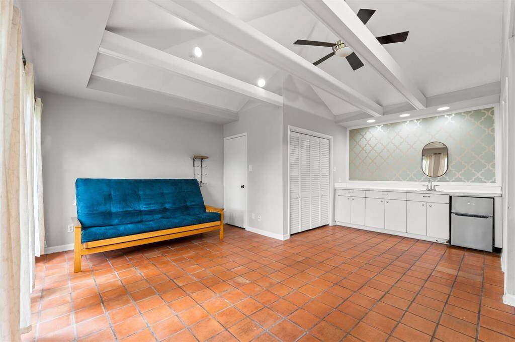 Converted garage/guest house features terracotta tile flooring, a beamed ceiling with a fan, a kitchenette with a mini fridge and ample cabinet space.