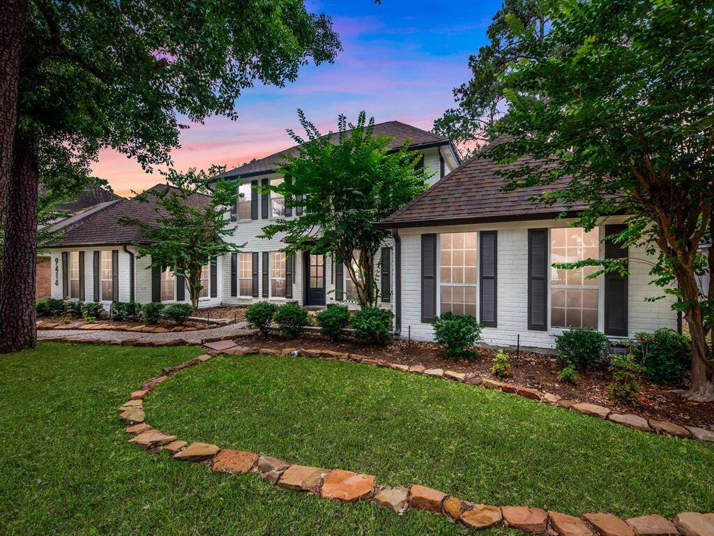 This charming home features a classic brick exterior with large windows and elegant shutters, surrounded by lush greenery and mature trees. The well-maintained front lawn includes a stone-bordered path, creating a welcoming and picturesque entrance.
