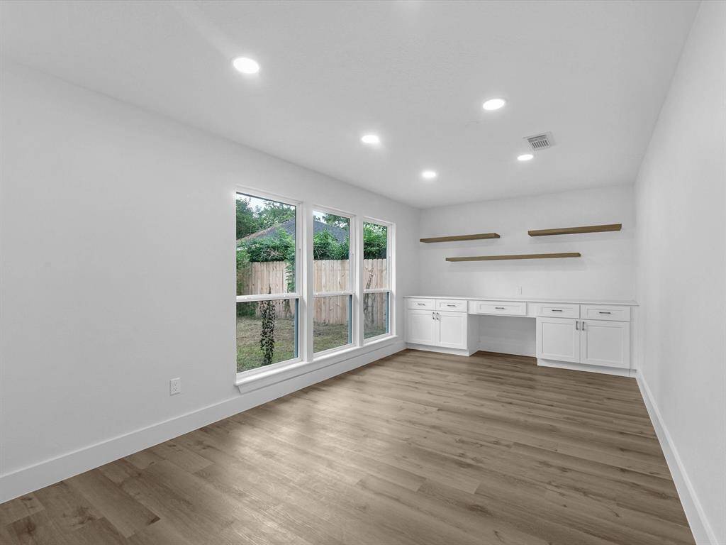 Bright, spacious room with large windows, hardwood floors, built-in shelving, and cabinets. Ideal for a home office or study.