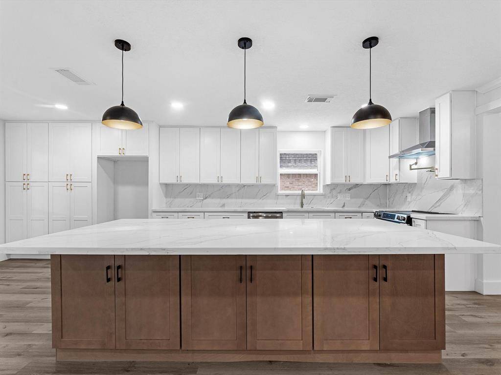This modern kitchen features a spacious marble island, sleek white cabinets, and stainless steel appliances. Pendant lights add a stylish touch, while ample storage and counter space enhance functionality.