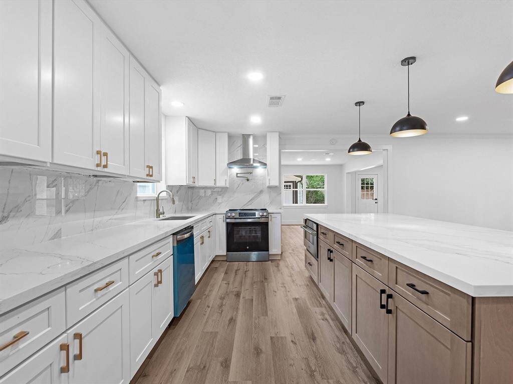 This modern kitchen features sleek white cabinetry, marble countertops, and a spacious island. It includes stainless steel appliances, wood flooring, and stylish pendant lighting, creating a bright and inviting space perfect for cooking and entertaining.