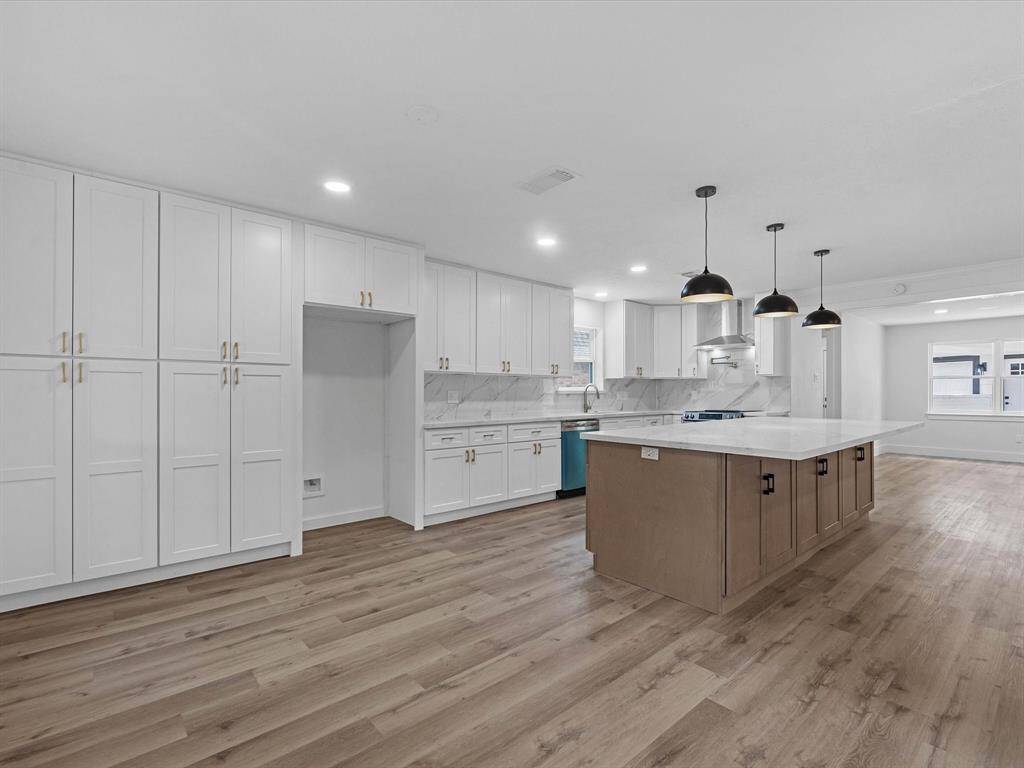 Spacious, modern kitchen with ample white cabinetry, a large island, and stylish pendant lighting. Features marble countertops, stainless steel appliances, and light wood flooring, creating an inviting and functional space.