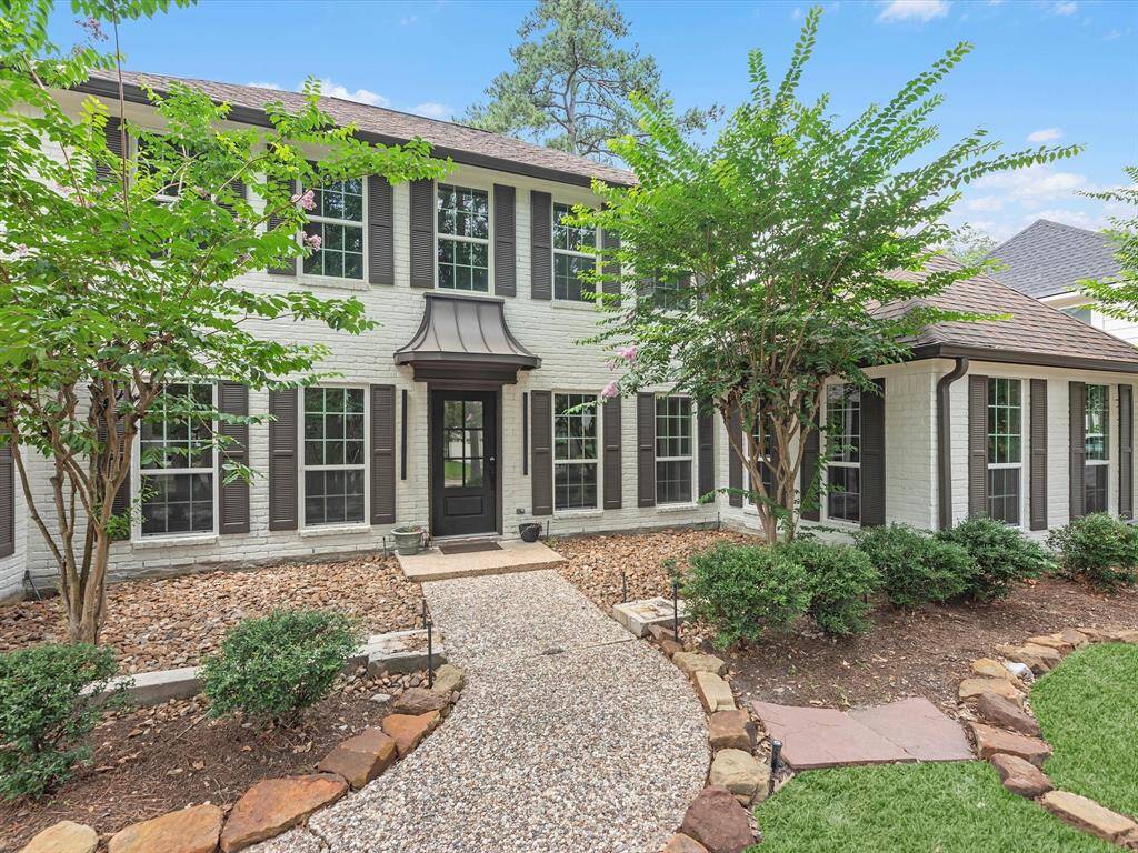 Charming two-story home with a classic brick exterior, large windows, and inviting landscaped front yard. Features a stone pathway leading to a welcoming entrance, surrounded by mature trees and well-maintained shrubs.